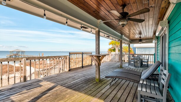 A wooden deck with a view of the ocean, a table, and two chairs.