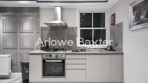 A modern kitchen with a gas stove, oven, and stainless steel range hood. - Hackney Suites - Triple En-suite Room (F2) (Greater London)