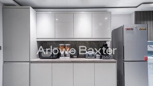 A modern kitchen with grey cabinets, a built-in microwave, a coffee maker, and a refrigerator. - Hackney Suites - Triple En-suite Room (F2) (Greater London)