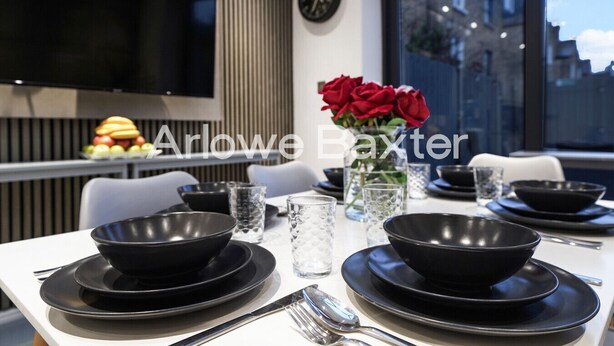 A dining table set with black bowls, plates, and cutlery, a vase with red roses, and a clock on the wall. - Hackney Suites - Single Room! (Greater London)