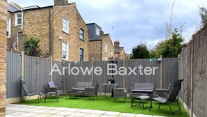 A patio area with a grey fence, outdoor furniture, and a well-maintained lawn. - Hackney Suites - Single Room! (Greater London)
