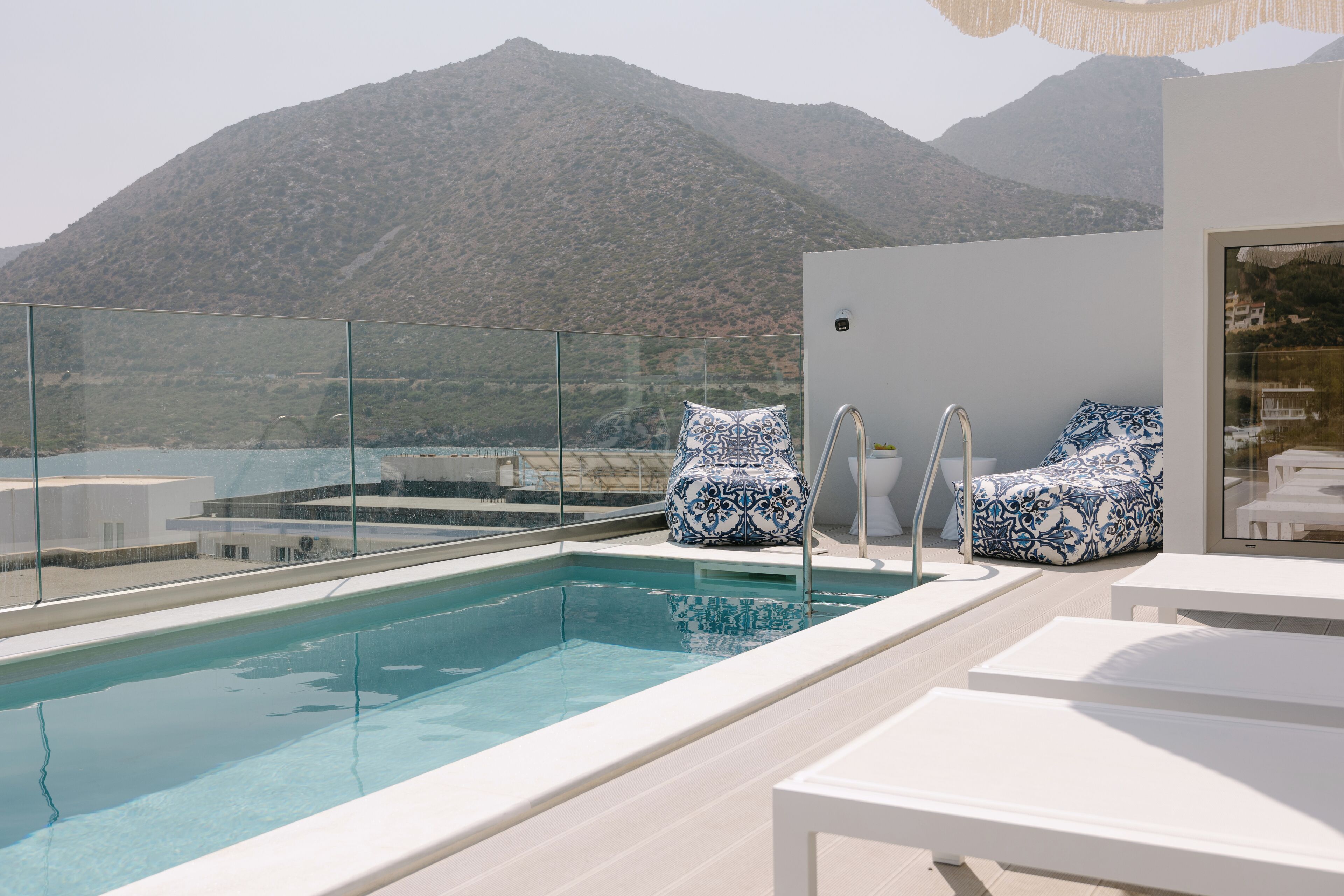 Un espace piscine offrant une vue sur les montagnes, doté d’une rambarde en verre et de chaises longues blanches.