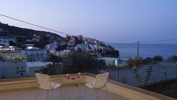 A balcony with two chairs and a table, overlooking a coastal town with buildings and a beach.