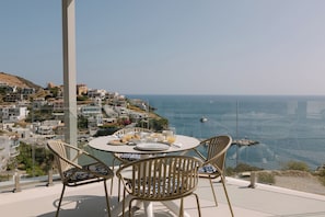 A table with chairs and a view of the sea and buildings.