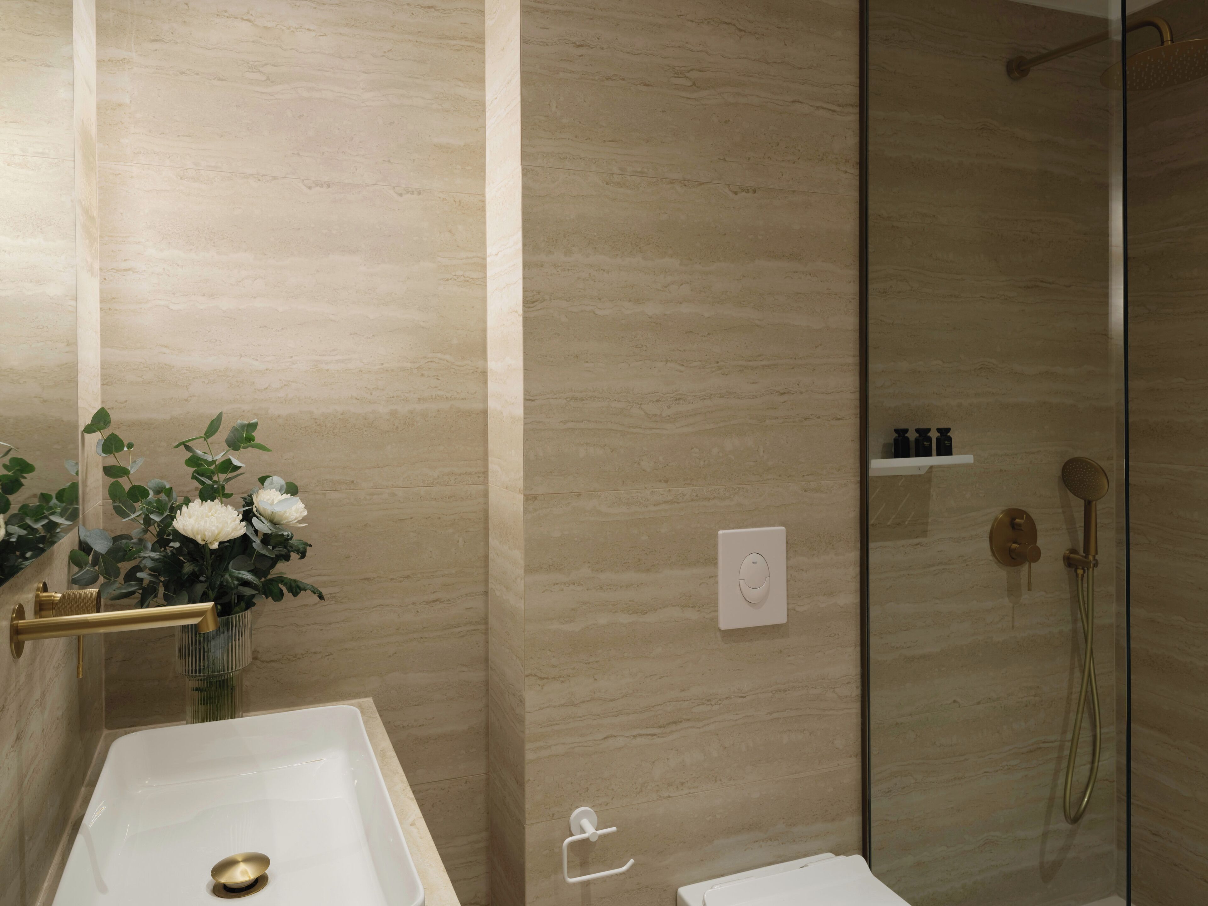 A bathroom with a bathtub, a shower, and a toilet. There is a vase with flowers on the left side.