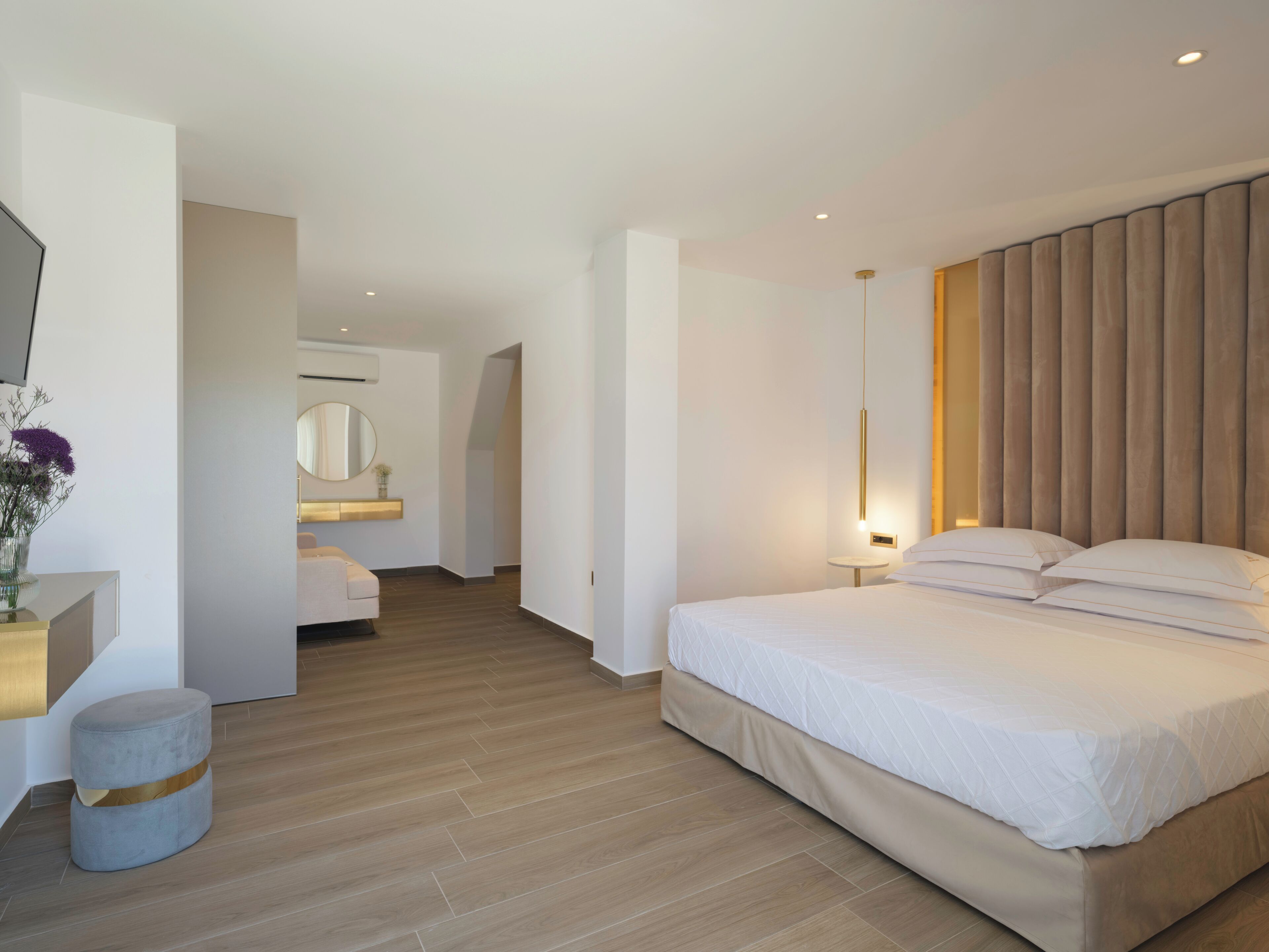 A modern hotel room with a large bed, a bedside table, a round mirror, a small round table, and a wall-mounted air conditioner.