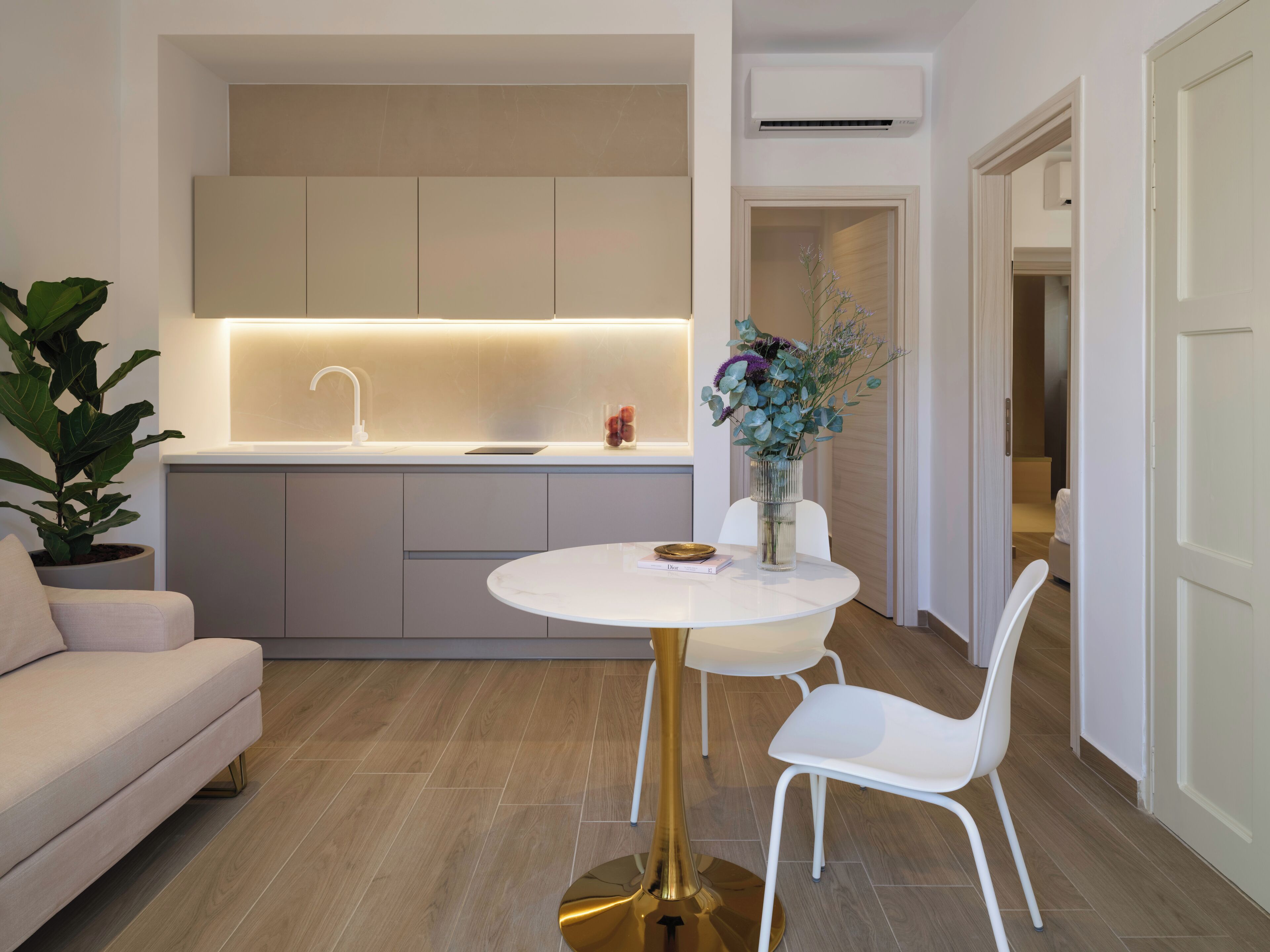 A modern kitchen with a white countertop, a sink, and cabinets. There is a dining area with a white table and chairs.