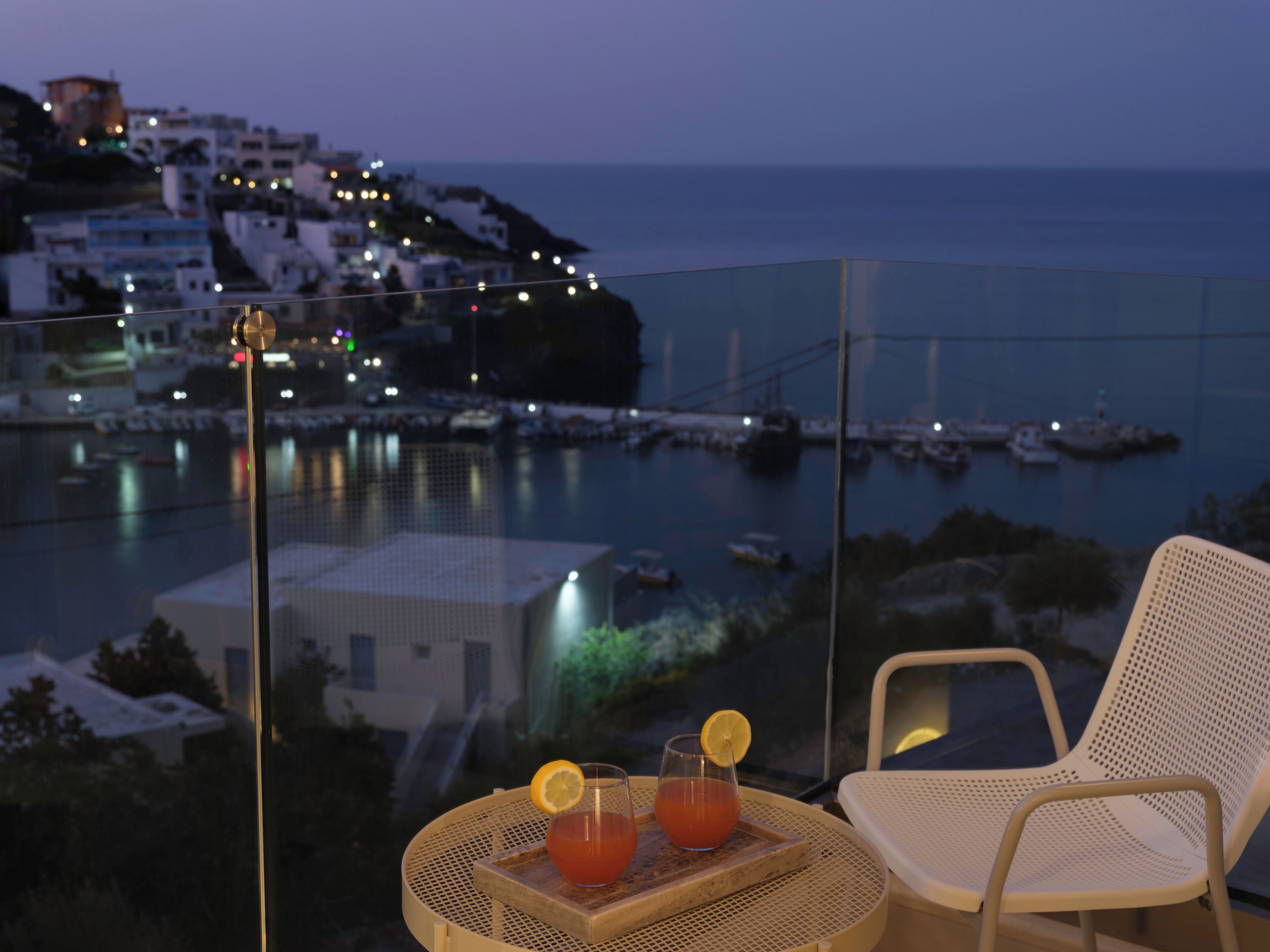 Un balcón con una mesa y una silla, con vista a un pueblo costero al atardecer.