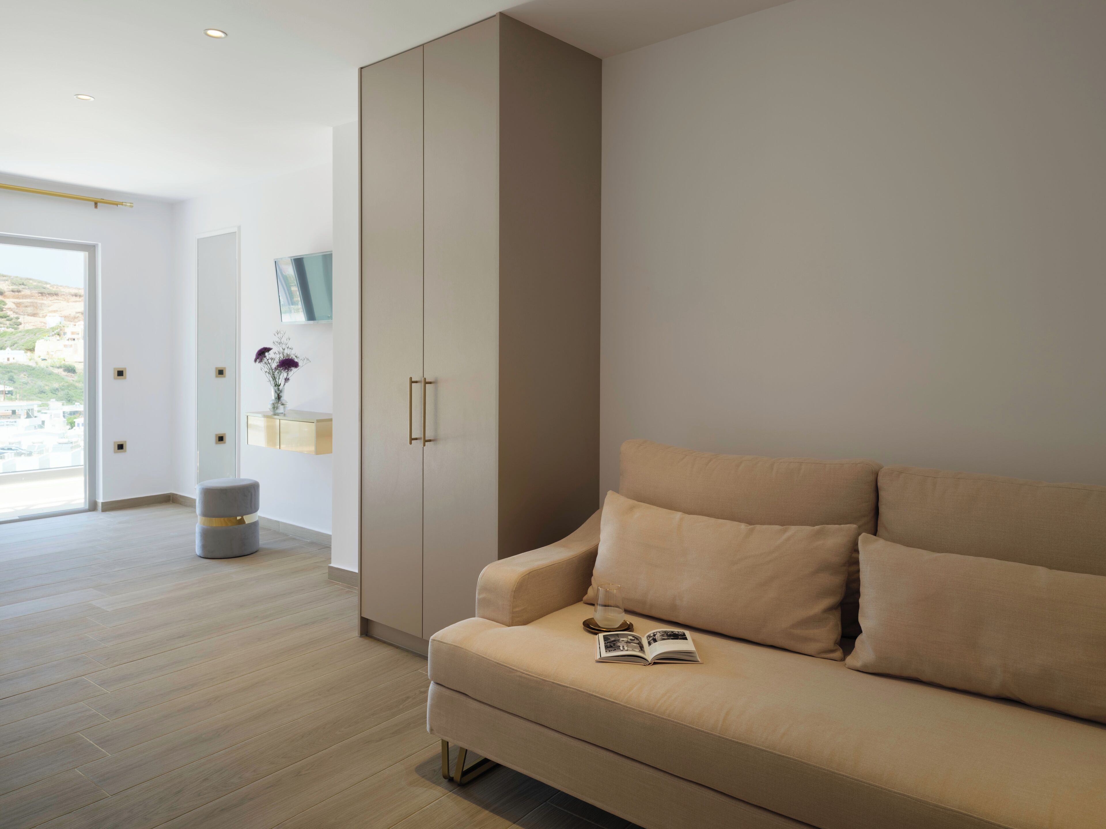 Un salon moderne avec un canapé beige, une grande armoire et un petit pouf rond.