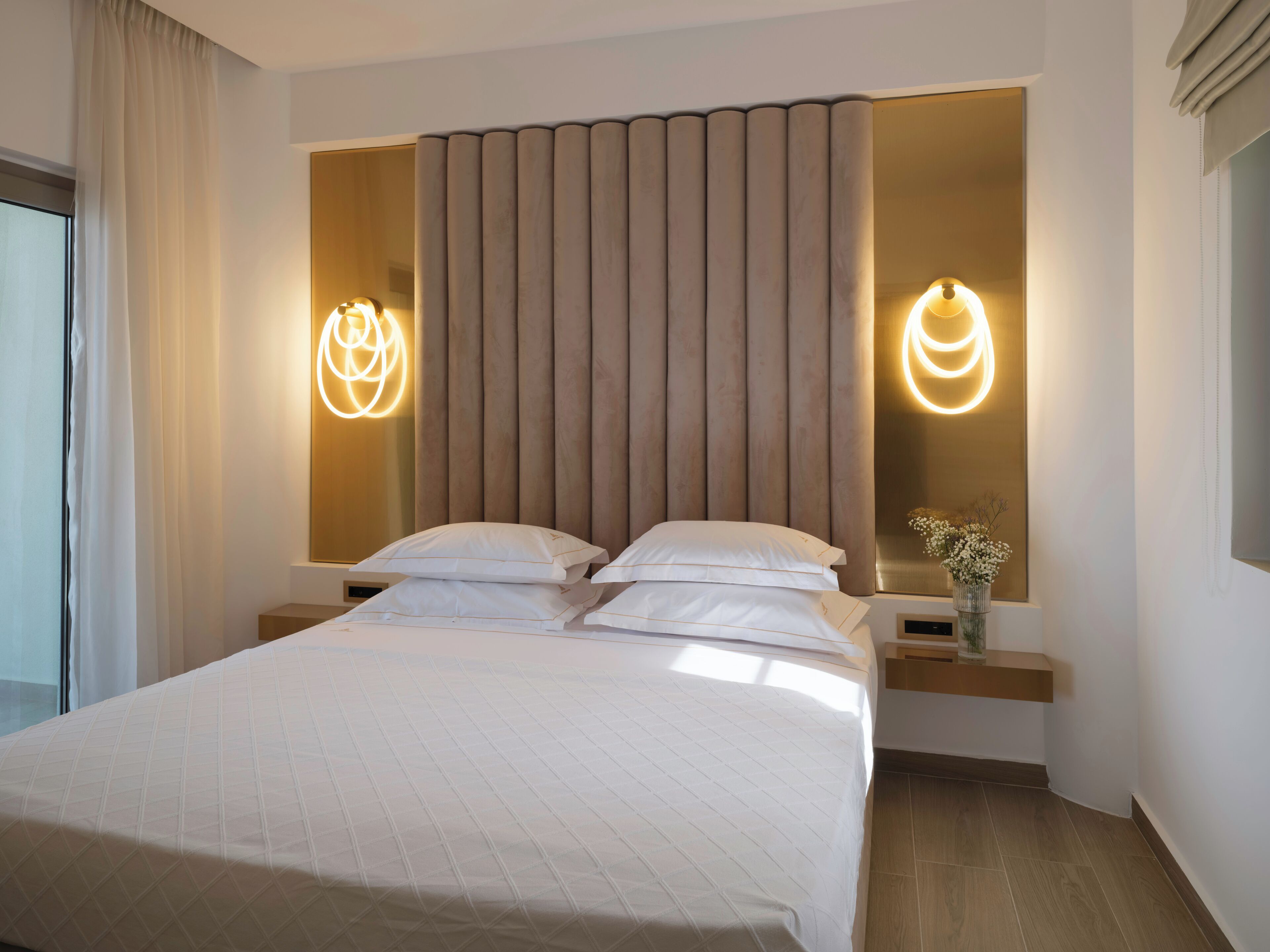 A modern hotel room with a large bed, two bedside tables, and a wall-mounted light fixture.