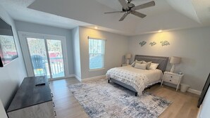 Une chambre à coucher comprenant un lit, des tables de chevet, un ventilateur de plafond, une fenêtre et une porte.