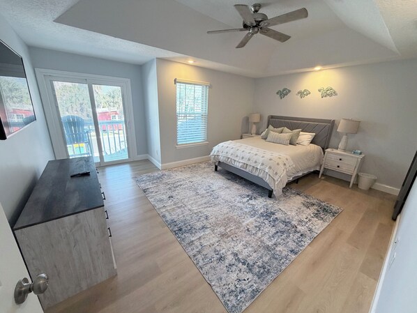 A bedroom with a bed, nightstands, a ceiling fan, a window, and a door.