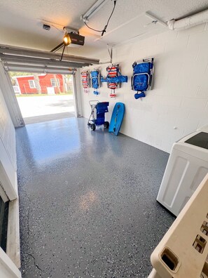 A garage with a concrete floor, a white washing machine, and several blue and red bags hanging on the wall.