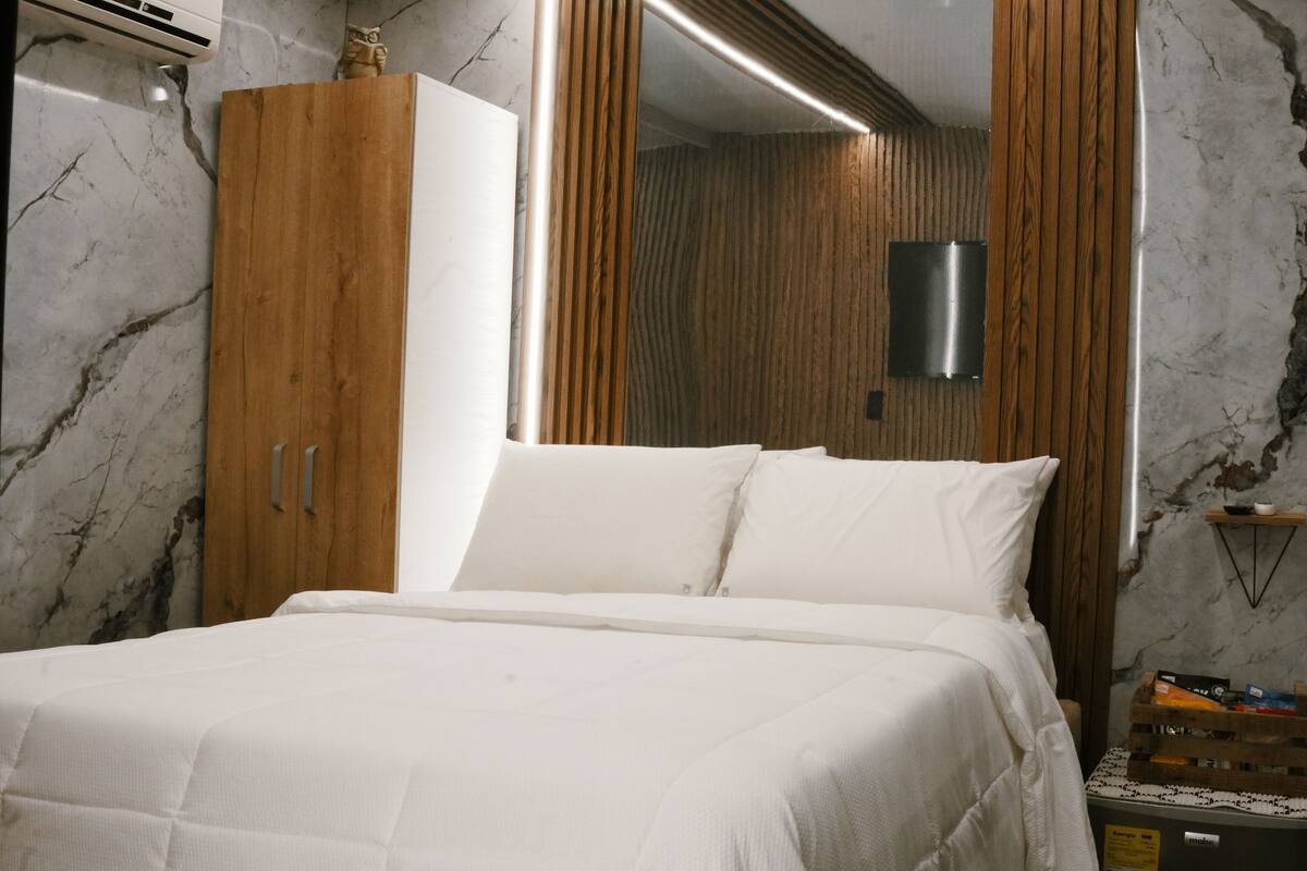 Ein Schlafzimmer mit Bett, Holzschrank und einem an der Wand befestigten Fernseher.