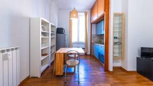 Una cocina estrecha con una mesa y sillas de madera, estanterías blancas y un armario azul.