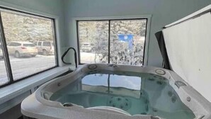 Ein Whirlpool in einem Raum mit großen Fenstern, einem Deckenventil und Blick auf geparkte Autos vor dem Haus.