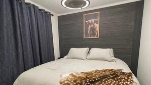 Ein Schlafzimmer mit einem Bett, dunklen Vorhängen, einem Kopfteil mit einem Gemälde und einer Deckenleuchte.