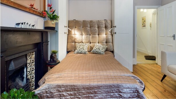 A bedroom with a large bed, a fireplace, and a door leading to another room. - Charming Apartment with Private Patio & Oak Finishes near Clapham Station (London)