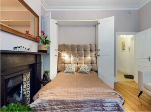 Een slaapkamer met een groot bed, een open haard en een deur naar een andere kamer.