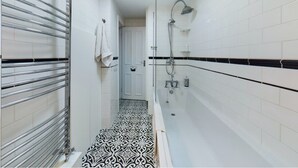 A narrow bathroom with a shower, a towel rack, and patterned floor tiles. - Charming Apartment with Private Patio & Oak Finishes near Clapham Station (London)