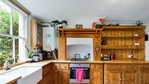A kitchen with wooden cabinets, a white countertop, a stove, and a window with plants. - Charming Apartment with Private Patio & Oak Finishes near Clapham Station (London)