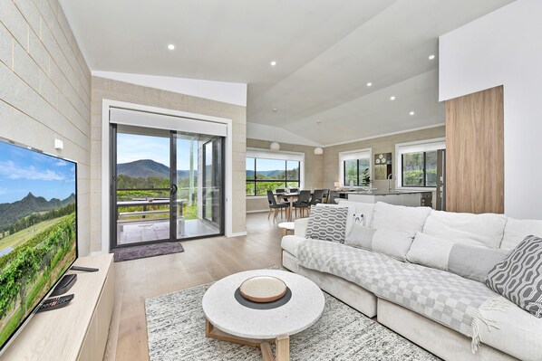 A modern living room with a flat-screen TV, a round coffee table, and a sofa with patterned cushions.