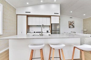 A modern kitchen with white cabinetry, a stainless steel refrigerator, and a central island with bar stools.