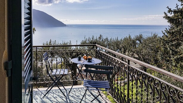 Un balcón con mesa y sillas que ofrece vistas panorámicas del mar y una montaña.
