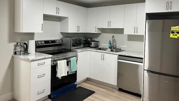 A modern kitchen with white cabinets, a stainless steel refrigerator, a built-in oven, and a microwave. - A Home away from Home
 (Dieppe)