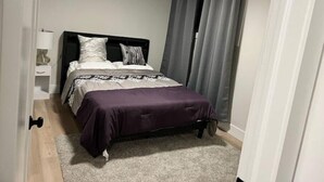 A bedroom with a bed, a nightstand, a lamp, and a window with curtains. - A Home away from Home
 (Dieppe)