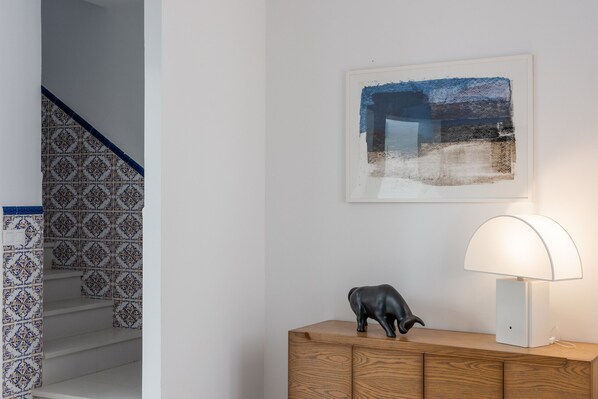 A staircase with patterned tiles, a wooden cabinet with a black sculpture, and a framed abstract painting.