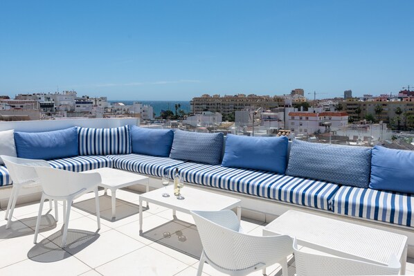 A rooftop terrace with a striped sofa, white chairs, and a table.