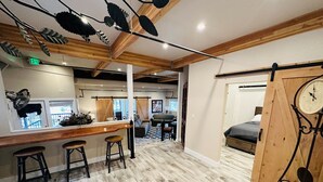 Ein modernes Interieur mit einer Holztresore, Barhocker, einem Bett mit Holztür und einer großen Uhr.