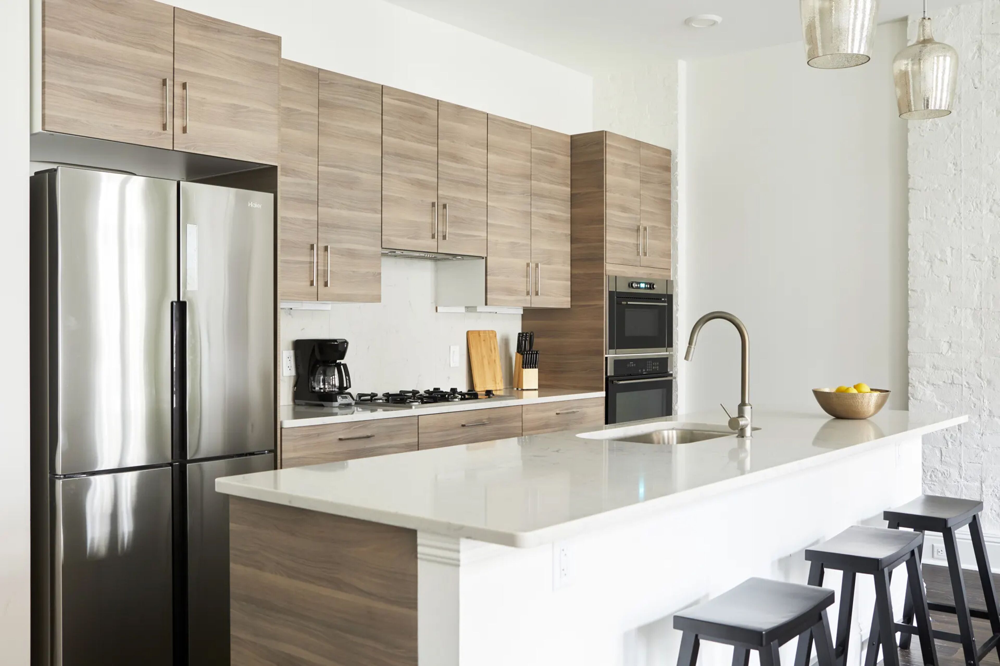 Una cocina moderna con electrodomésticos de acero inoxidable, armarios de madera y una isla blanca con taburetes de bar.