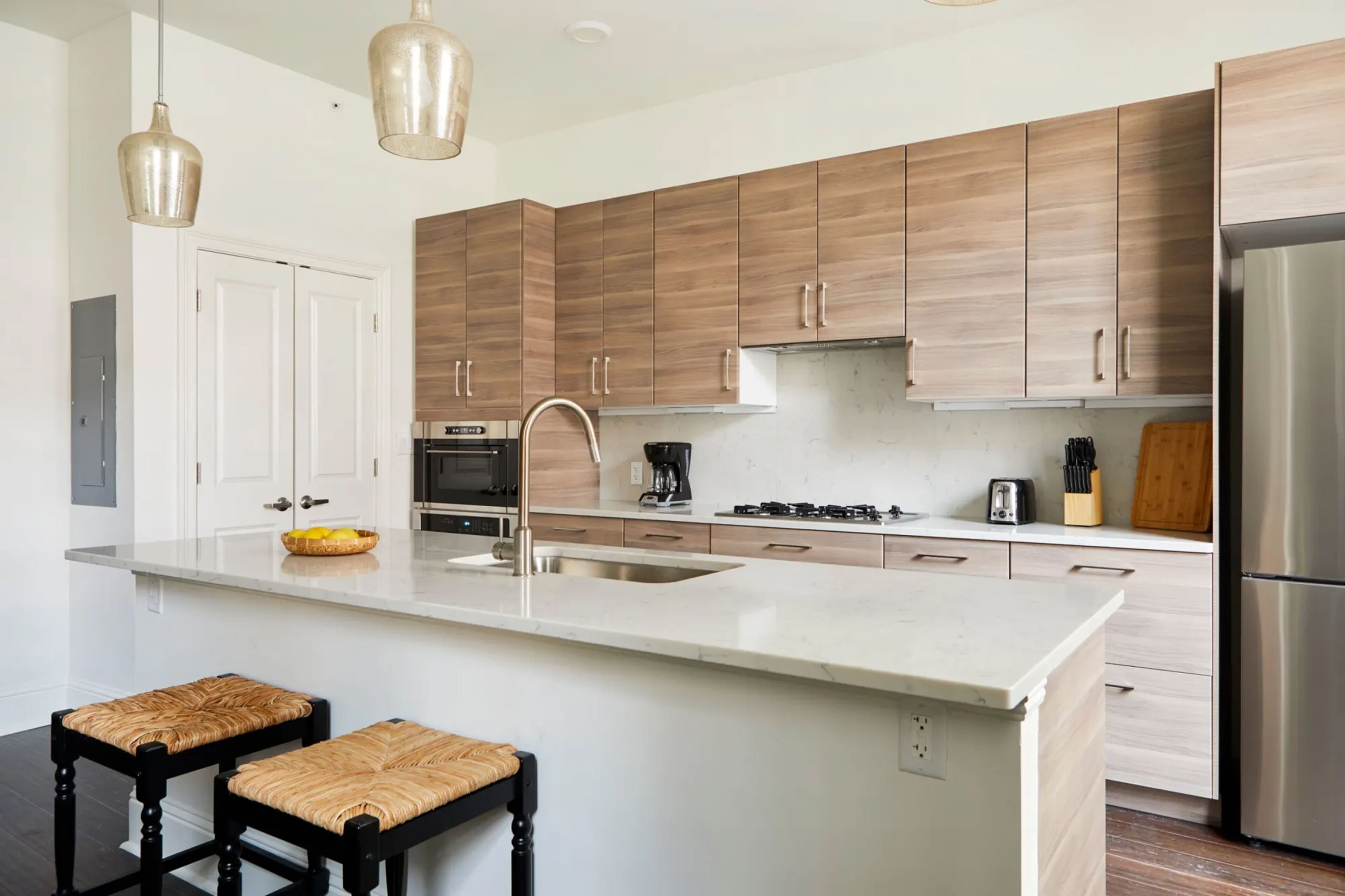 Una cocina moderna con armarios de madera, un refrigerador de acero inoxidable y una isla central con taburetes.