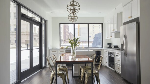 Une cuisine moderne avec une table à manger, des chaises, un lustre et une grande fenêtre.