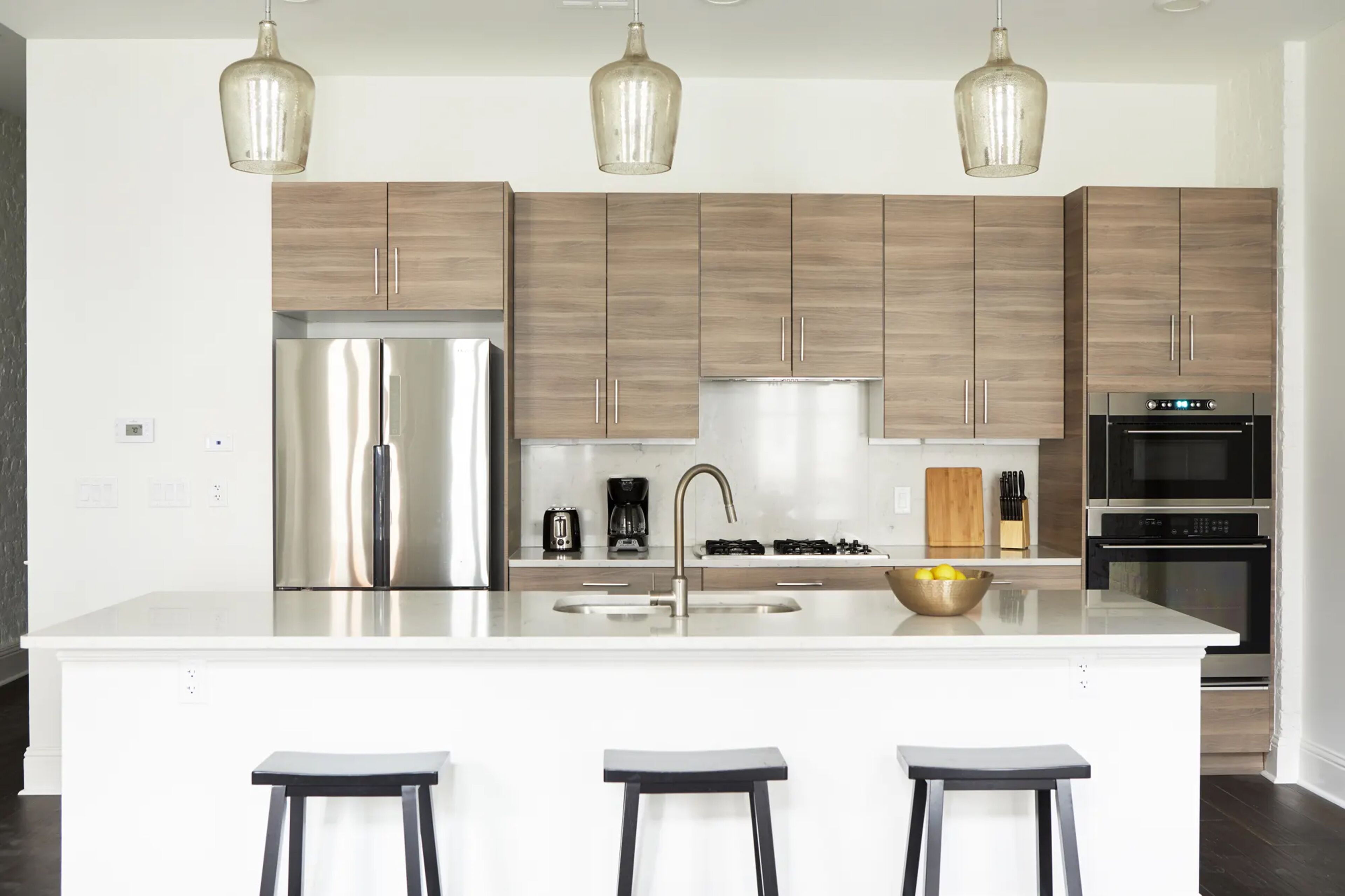 Una cocina moderna con una isla central, electrodomésticos de acero inoxidable, armarios de madera e iluminación colgante.