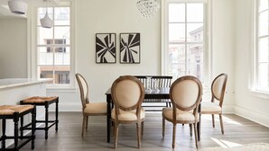 Un coin repas avec une table noire et quatre chaises, deux tableaux abstraits en noir et blanc accrochés au mur, et un lustre.
