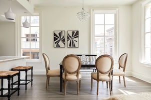 Un comedor con una mesa negra y cuatro sillas, dos cuadros abstractos en blanco y negro en la pared, y una araña.