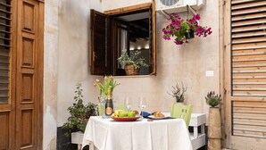 An outdoor dining area with a table set for two, featuring a bottle of champagne, a bowl of fruit, and a croissant. - Surrounded by the sea in Ortigia vacation home Syrakosia (Siracusa)