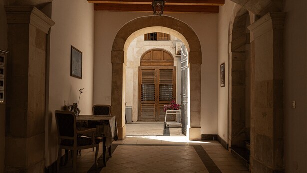 A corridor with a tiled floor, wooden door, and a table with chairs. - Surrounded by the sea in Ortigia vacation home Syrakosia (Siracusa)