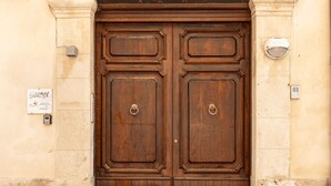 A large wooden double door with a metal handle, set in a beige stone wall. - Surrounded by the sea in Ortigia vacation home Syrakosia (Siracusa)
