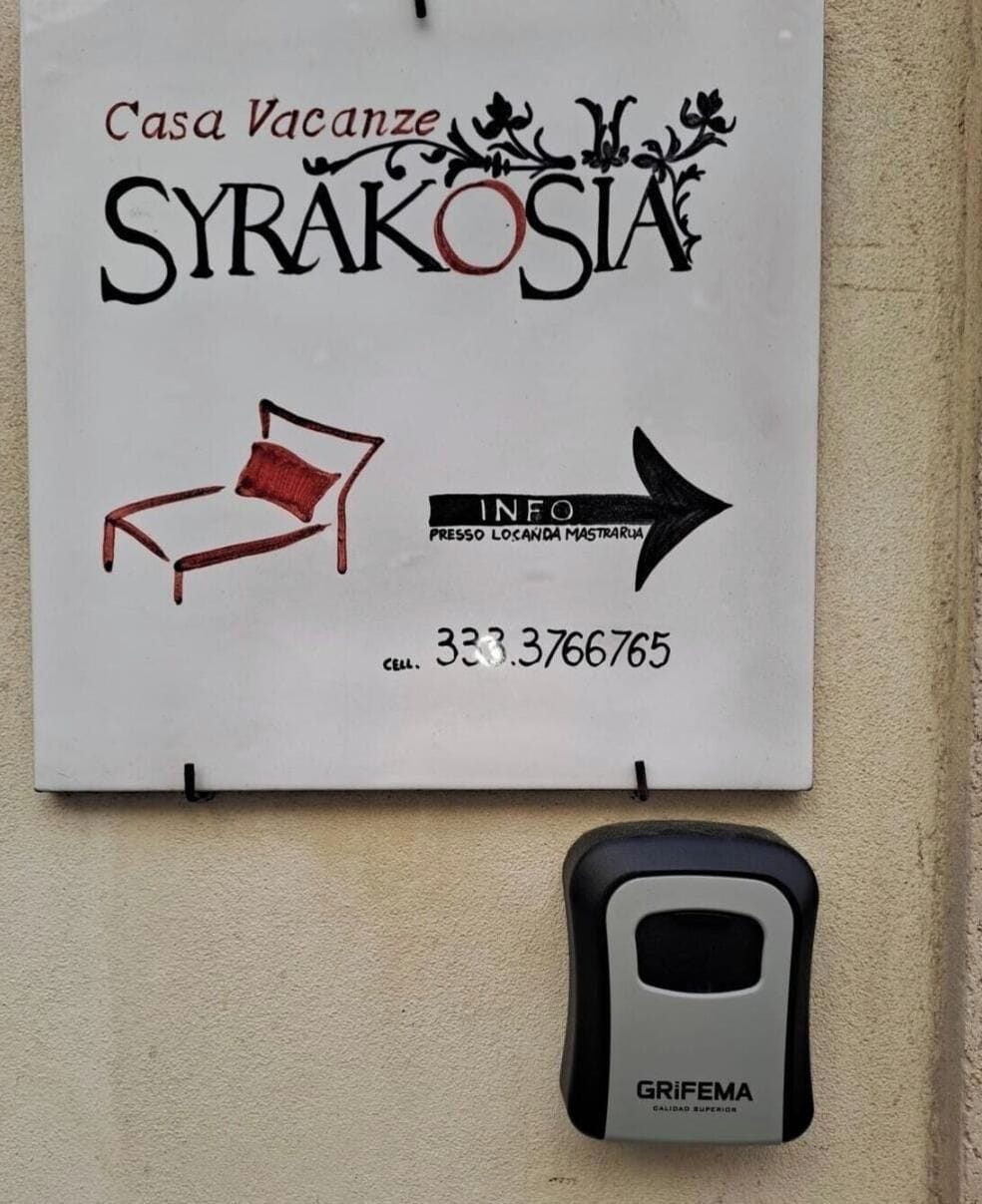 Een bordje met 'Casa Vacanze SYRAKOSIA', een telefoonnummer en een informatiepijl.