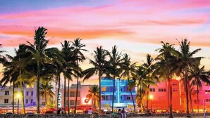 A beachside hotel with palm trees, colorful buildings, and a sunset sky. - Luxury Waterfront Suite with Great Views (Hallandale Beach)