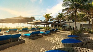 A beachside lounge area with sun loungers and umbrellas, surrounded by palm trees and a building in the background. - Luxury Waterfront Suite with Great Views (Hallandale Beach)