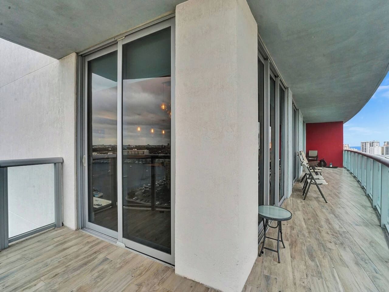 Un balcon donnant sur un paysage urbain, un mur rouge et une porte vitrée menant à un espace intérieur.