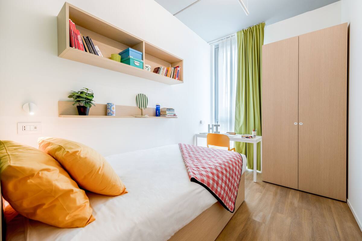 A modern bedroom with a bed, a desk, shelves, and a wardrobe.