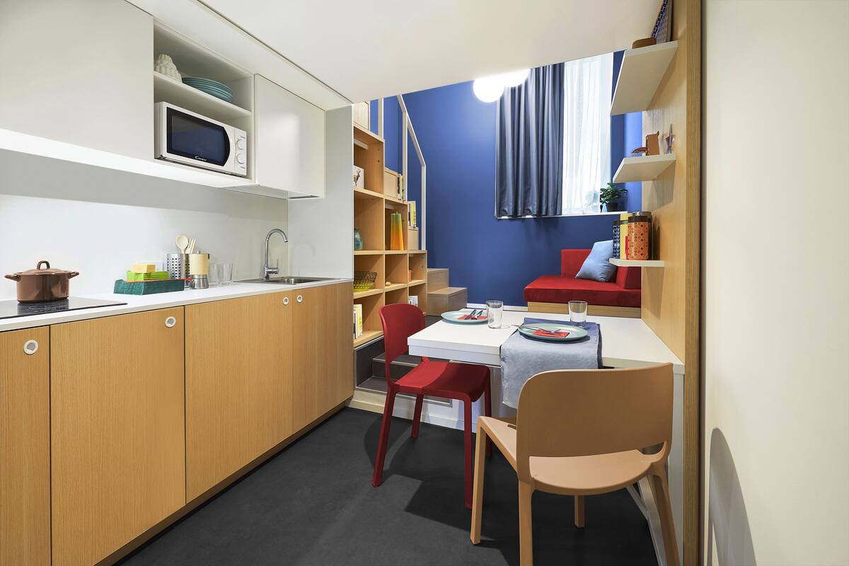 A compact kitchen with wooden cabinets, a microwave, and a dining area with a table and chairs.