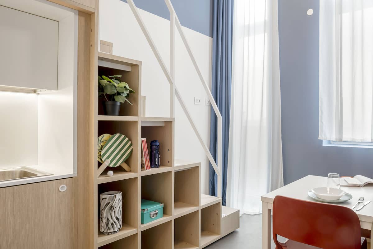 A modern room with a built-in bookshelf, a dining area with a table and chairs, and a staircase.