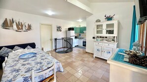 A well-lit room with a bed, a dining table, a kitchen area, and a staircase.